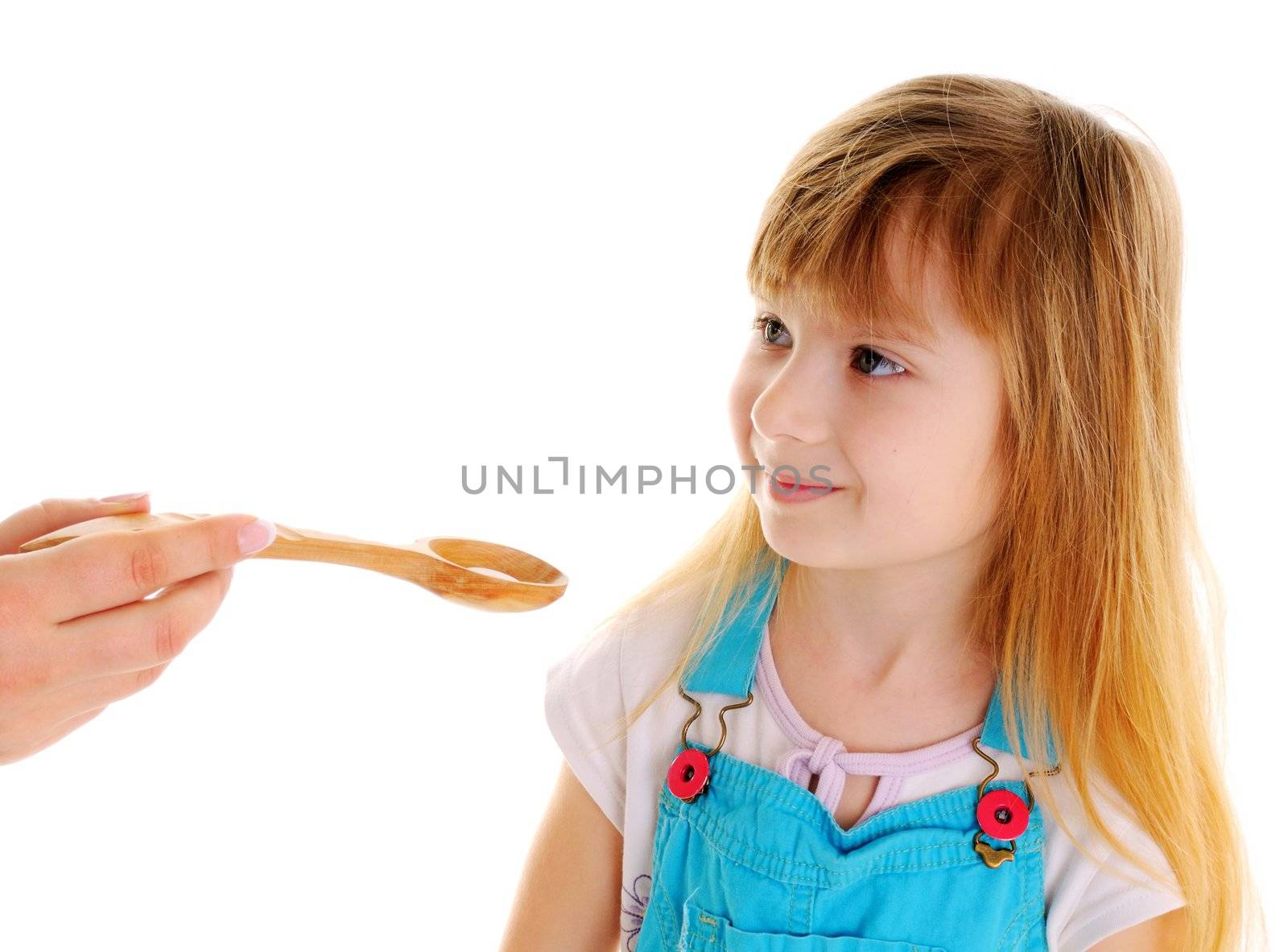 Small beauty girl is taking a white tablet in wooden spoon from female hand on white background