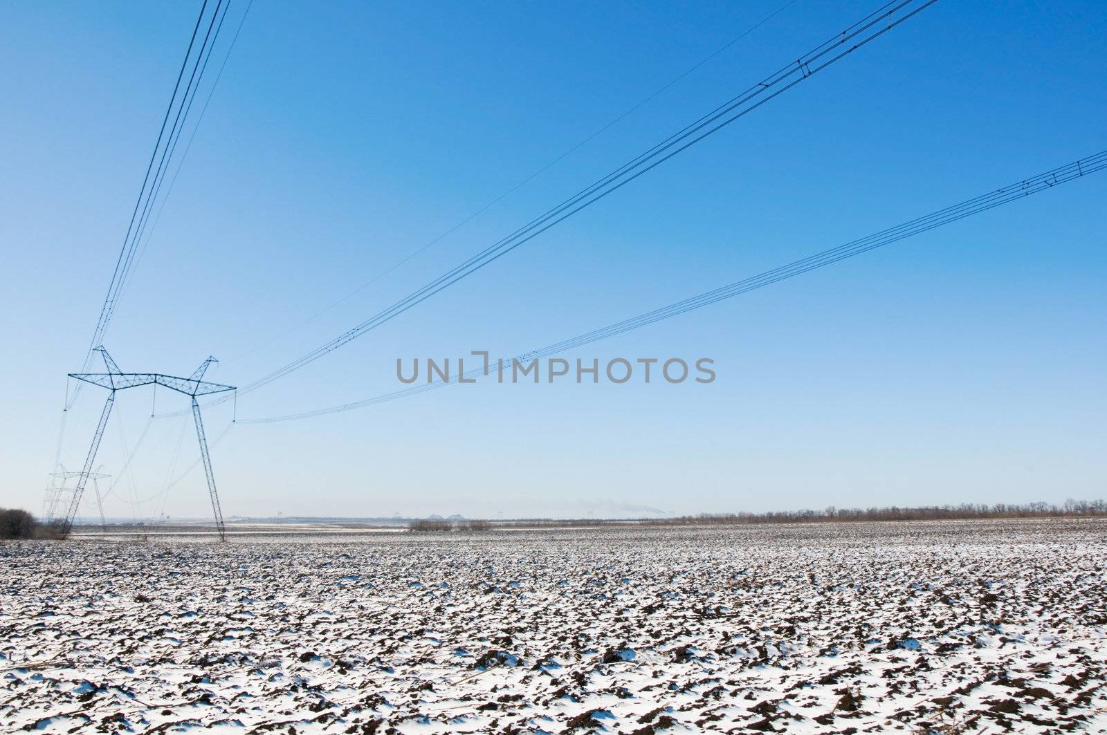 Line of electric pylons and long caples on winter snow-covered field