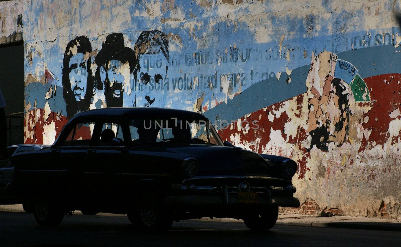 American taxi car on the street in Havana, Cuba. Behind a car painted wall with images of Che Gevarra,Fidel Castro and propaganda words
