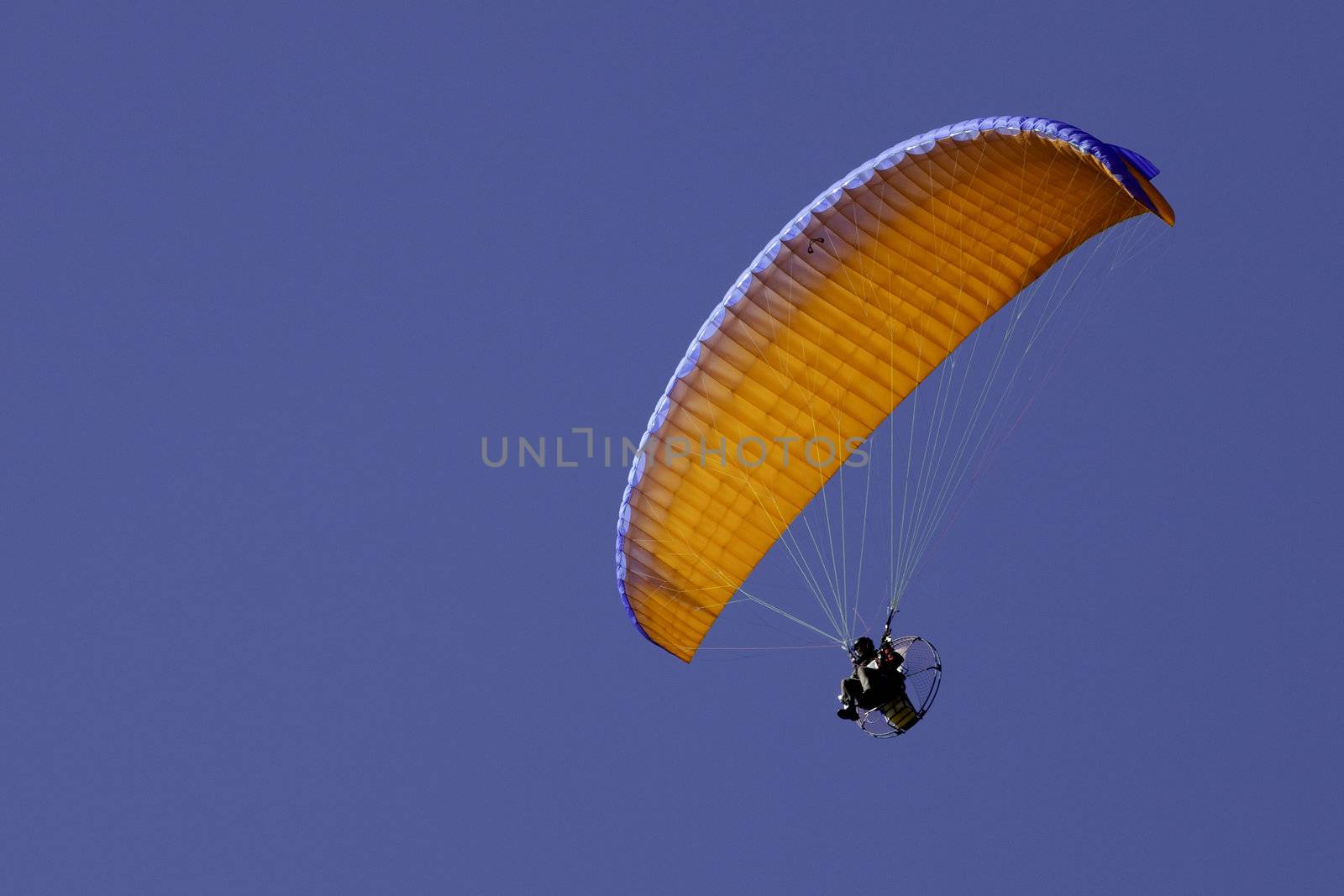 Orange powered paraglide or paramotor against blue sky
