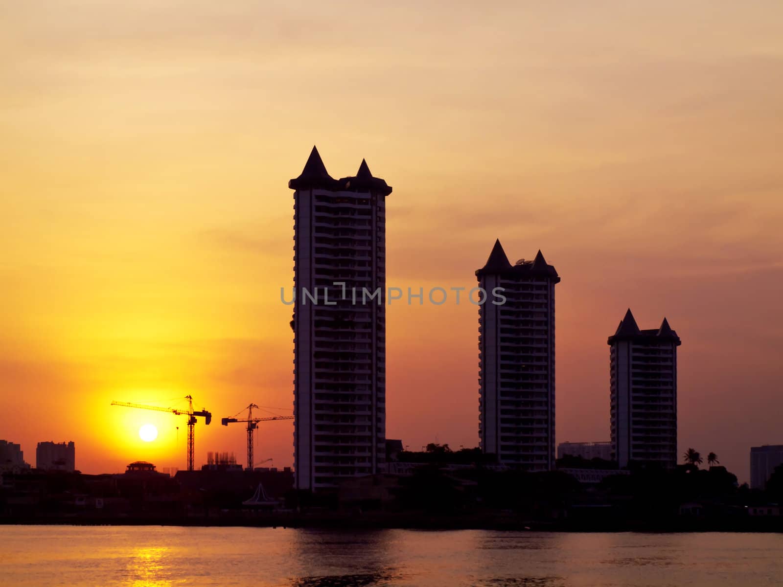 Buildings with construction site and river silhouette in the orange sunset