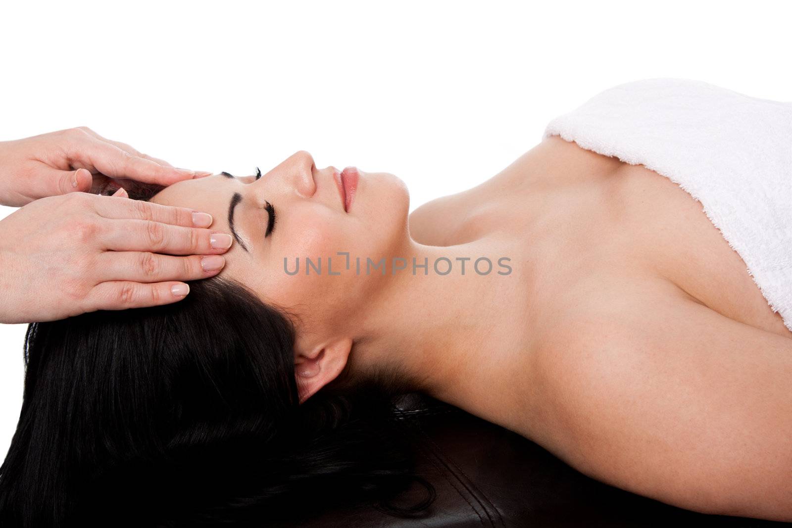 Beautiful happy young woman at day spa getting facial massage beauty treatment laying in white towel, isolated.