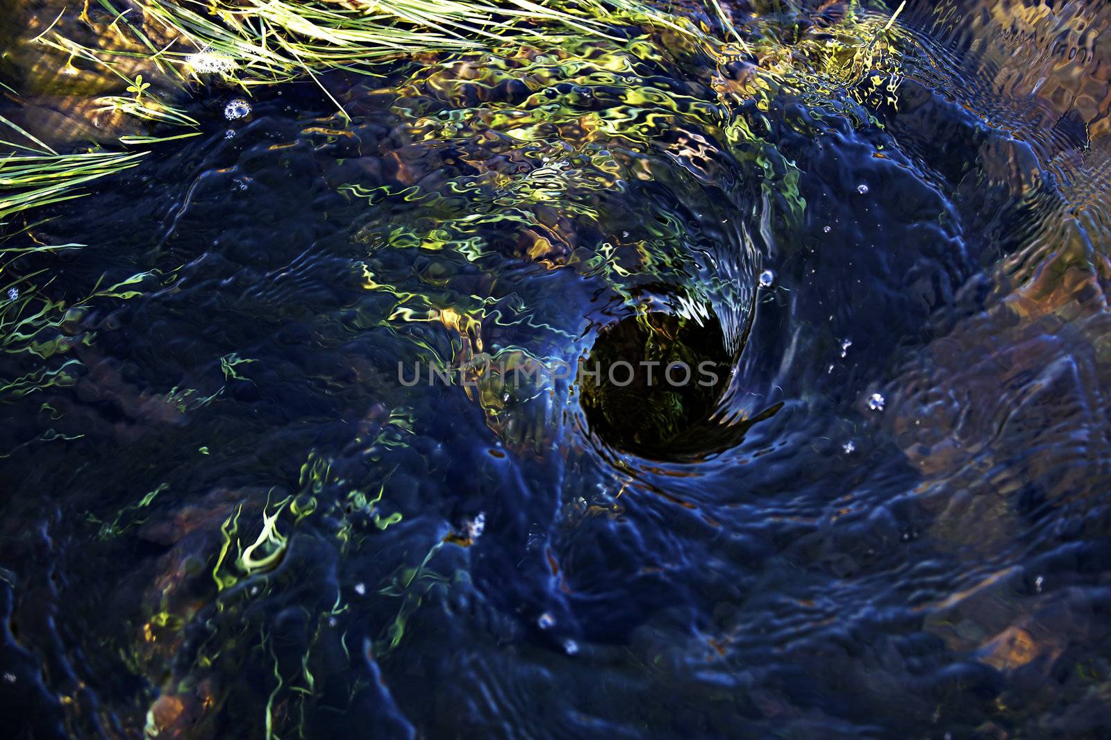 Blue water swirling down a hole in the ground