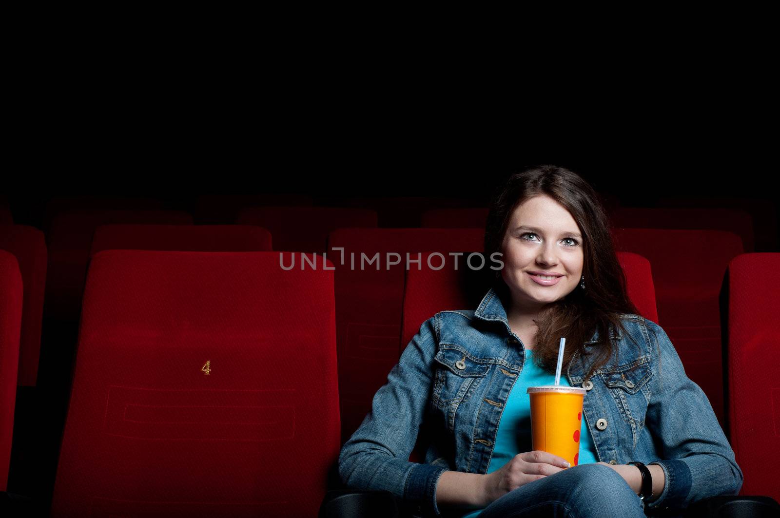 beautiful woman in a movie theater, watching a movie and drink a drink