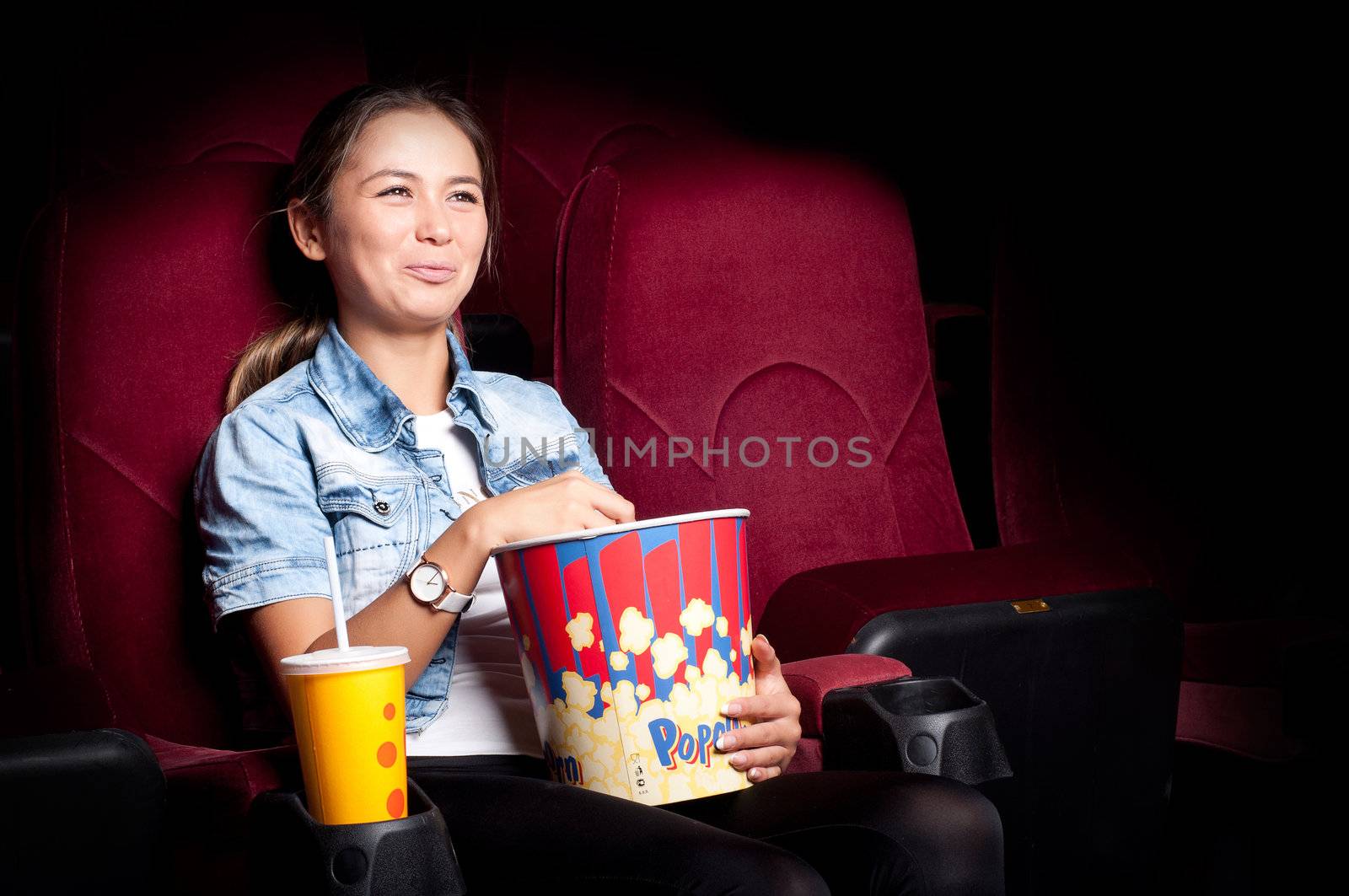 beautiful woman in a movie theater, watching a movie and drink a drink