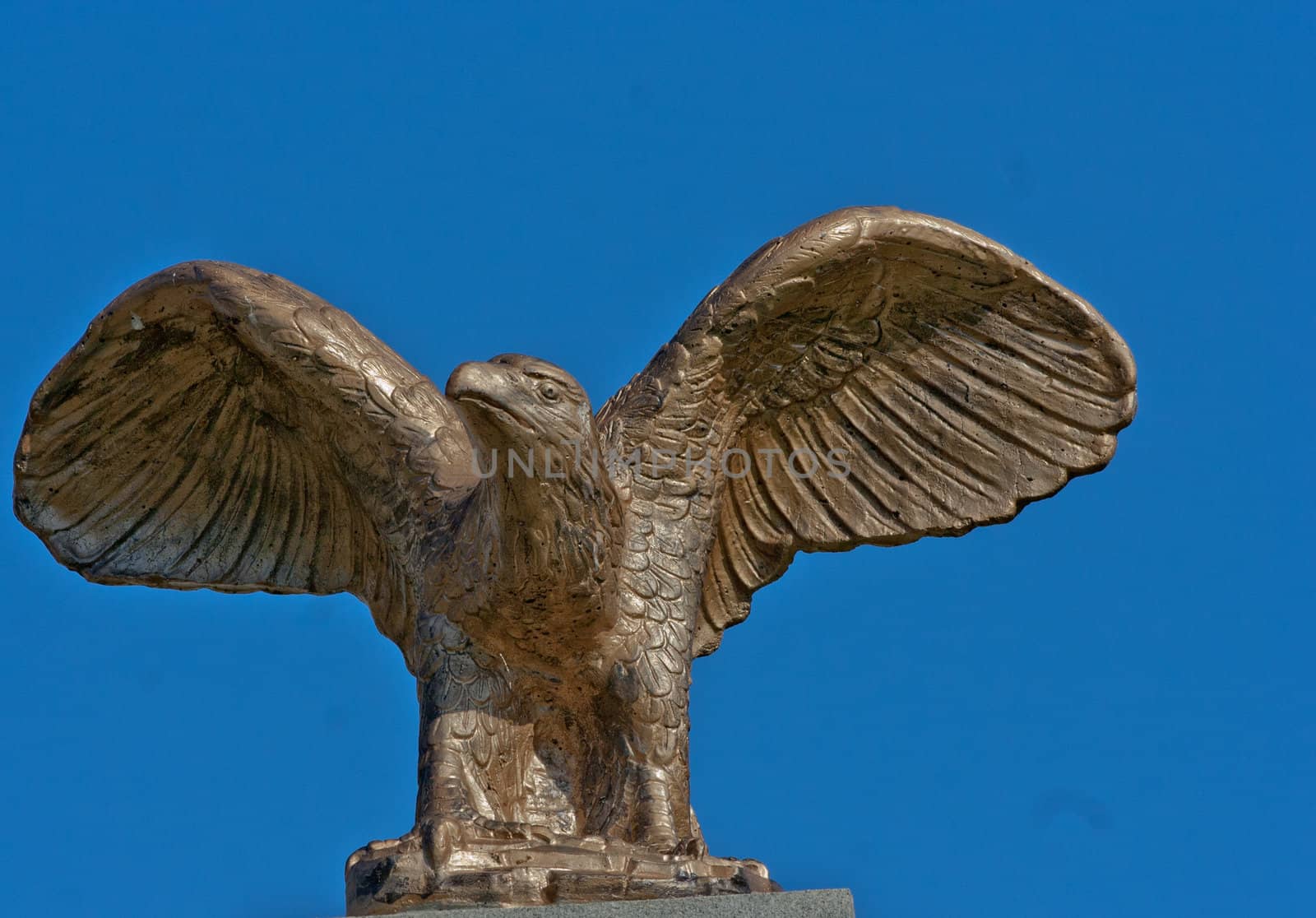 Eagle in flight as a bronze statute against a blue sky.