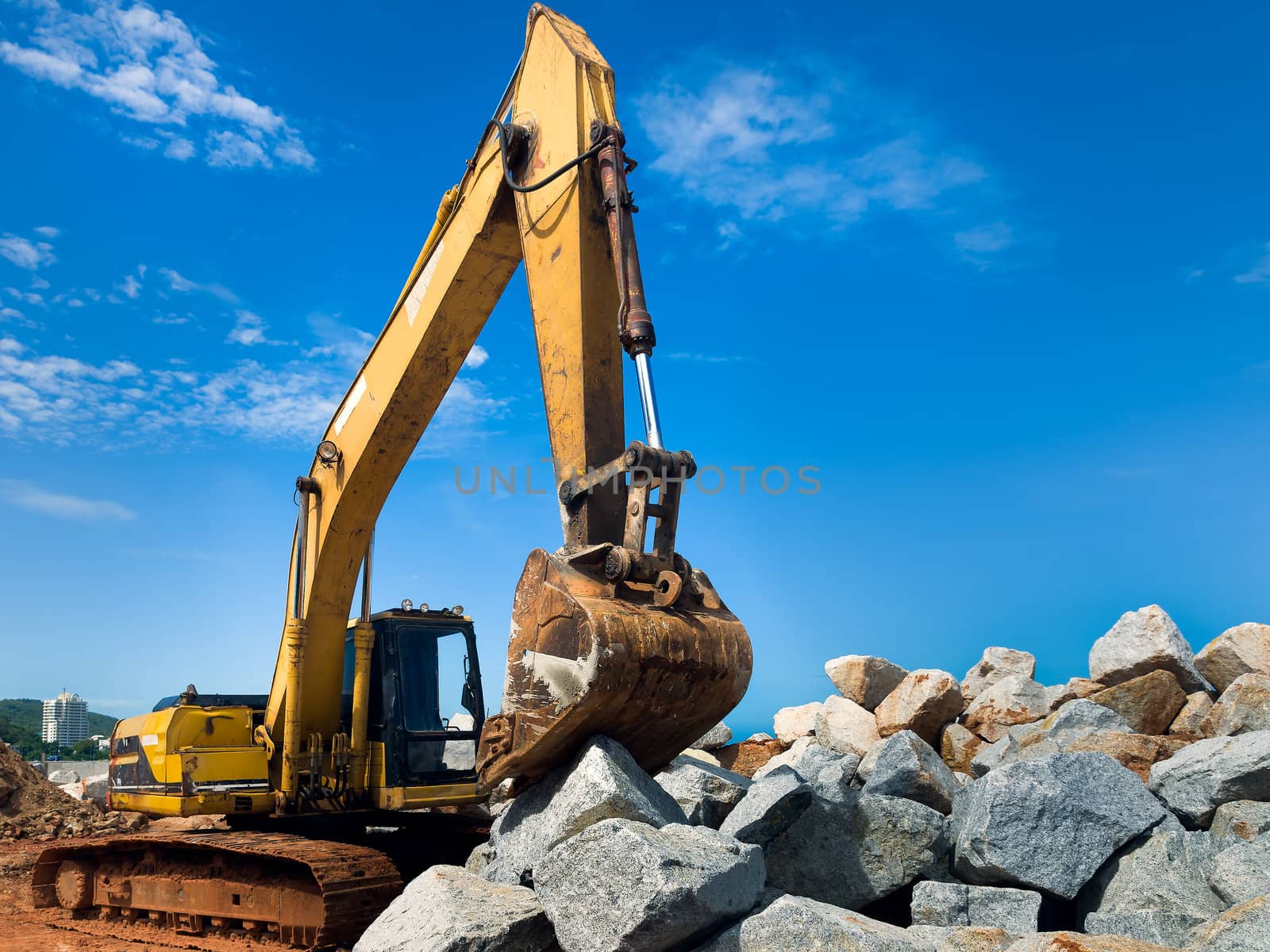 Yellow tracked excavator working on a large pile of rock