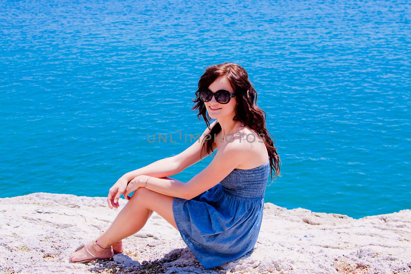 Young and beautiful girl resting on rocks against the sea