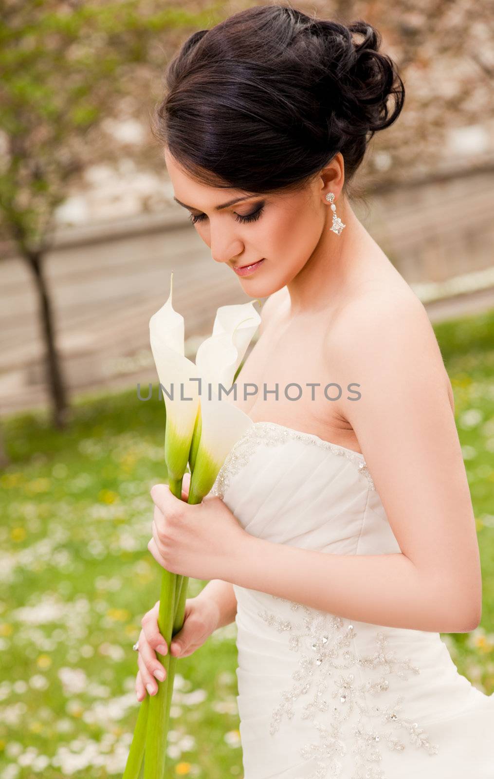 Beautiful bride with wedding dress holding white calla lilies looking down