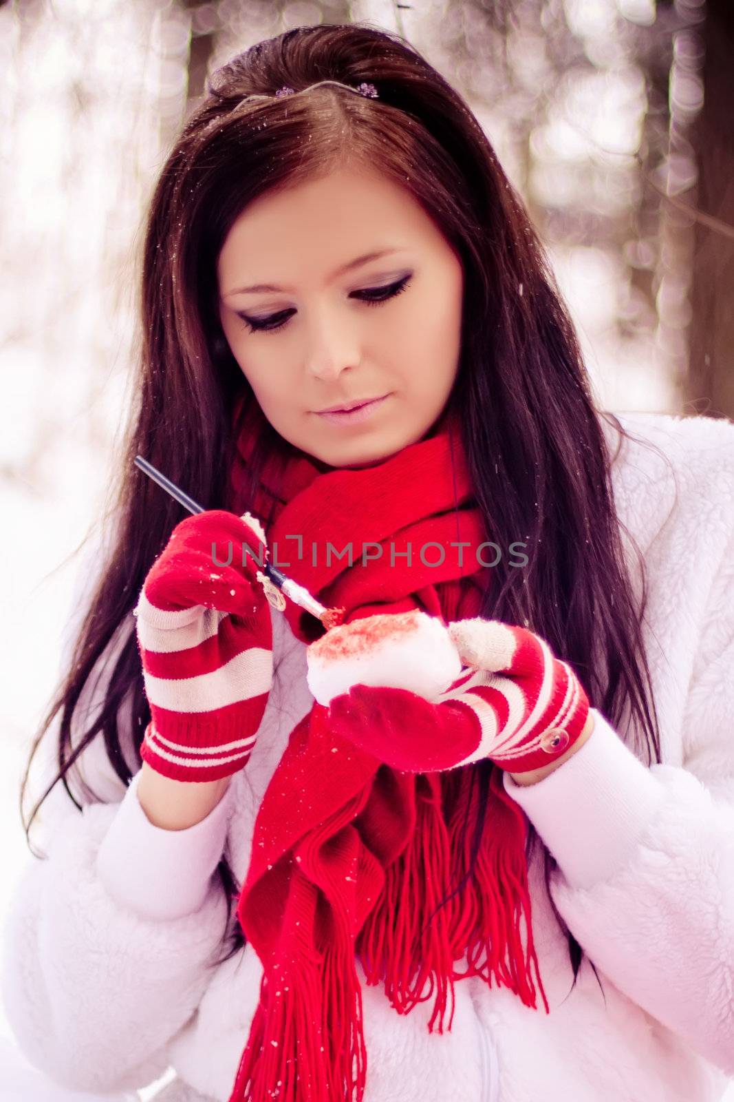 Young beautiful girl in the snow white forest painting heart in red.