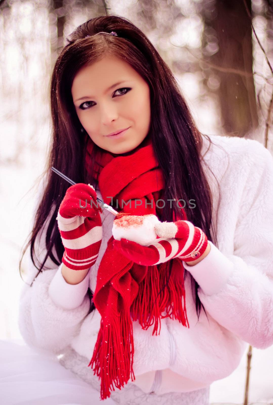 Young beautiful girl in the snow white forest painting heart in red.