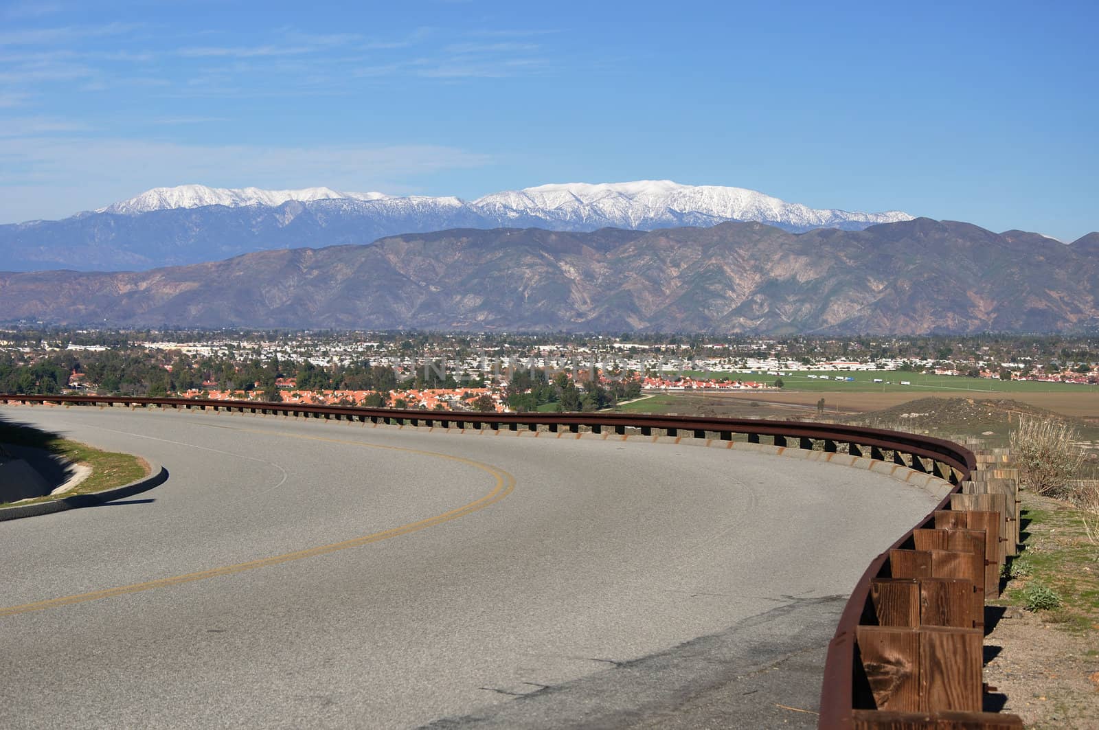 A curving road overlooks the town of Hemet, California with snow-capped Mount San Gorgonio in the background.