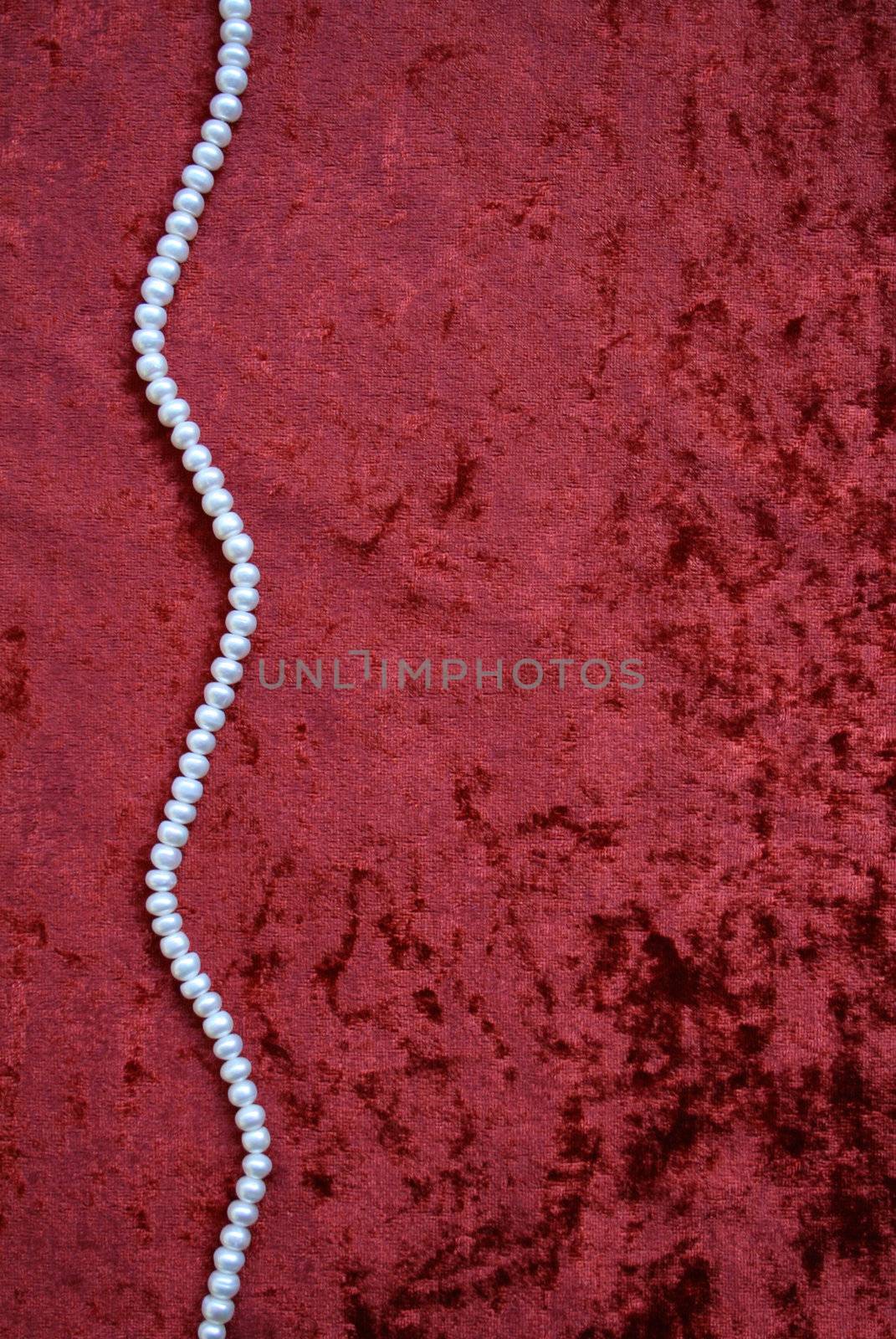 Necklace of white pearls on a terracotta velvet as background 