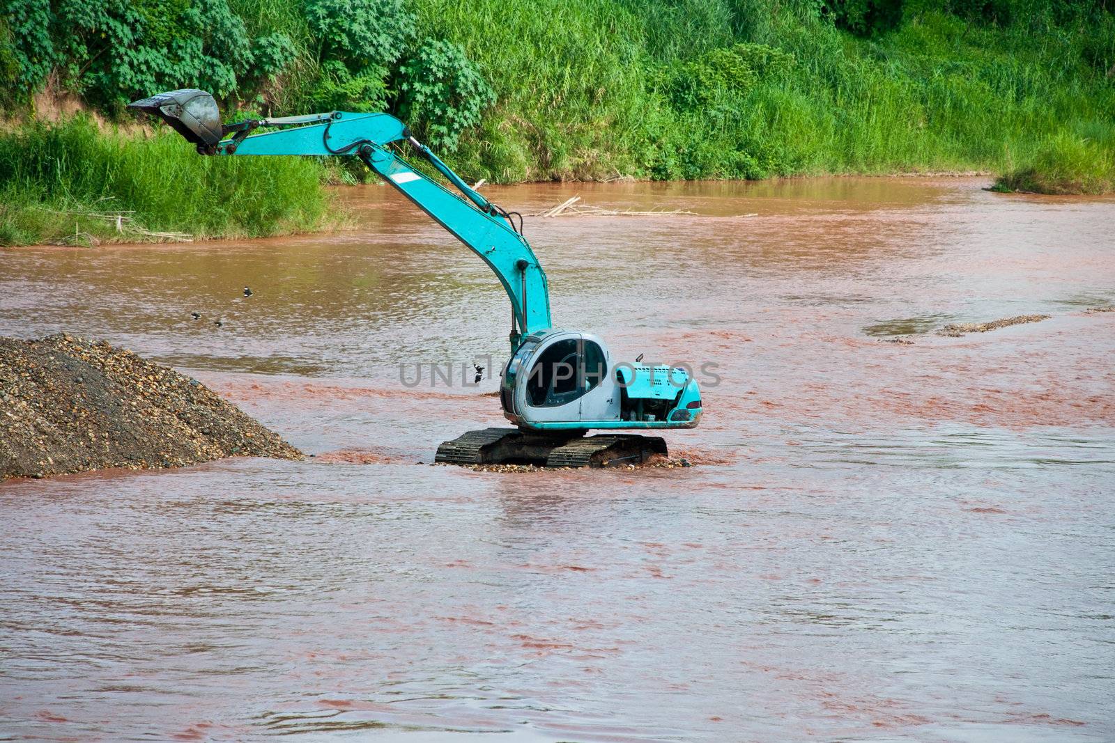 Excavator loader at river with raised bucket over blue sky by Yuri2012