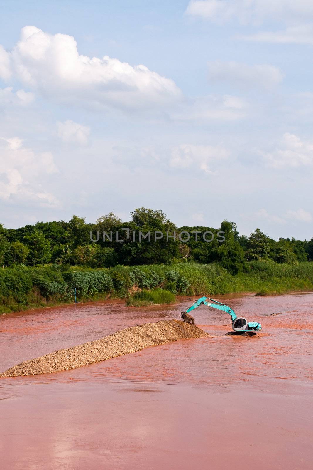 Excavator loader at river with raised bucket over blue sky by Yuri2012