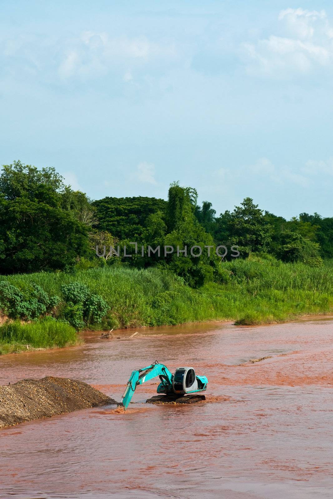 Excavator loader at river with raised bucket over blue sky