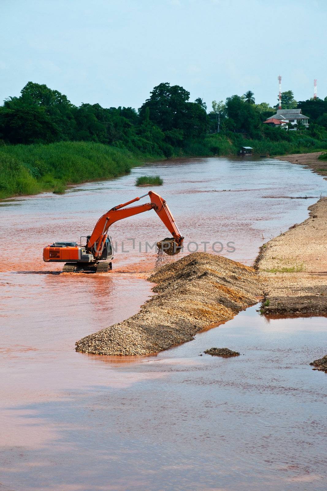 Excavator loader at river with raised bucket over blue sky