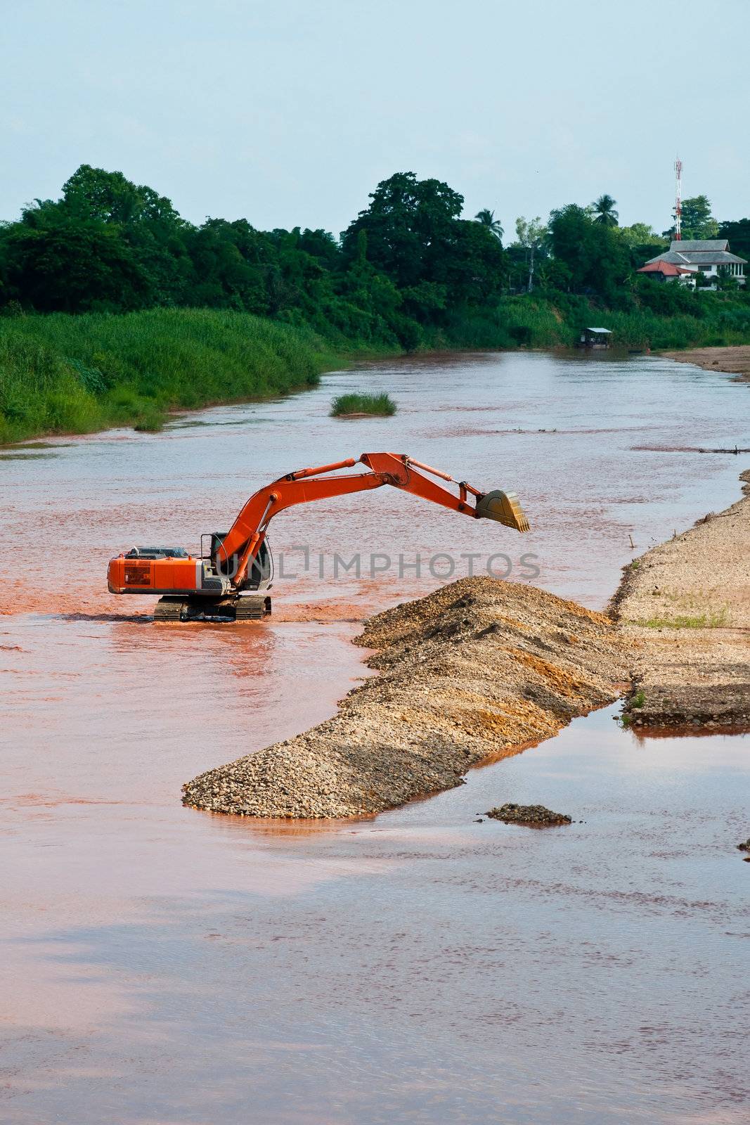 Excavator loader at river with raised bucket over blue sky by Yuri2012