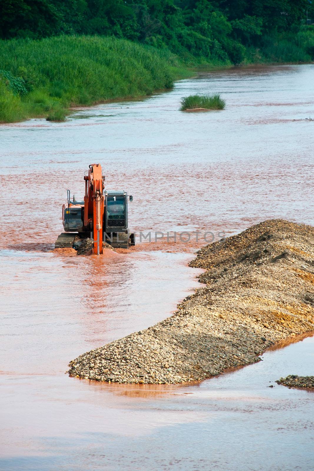 Excavator loader at river with raised bucket over blue sky by Yuri2012