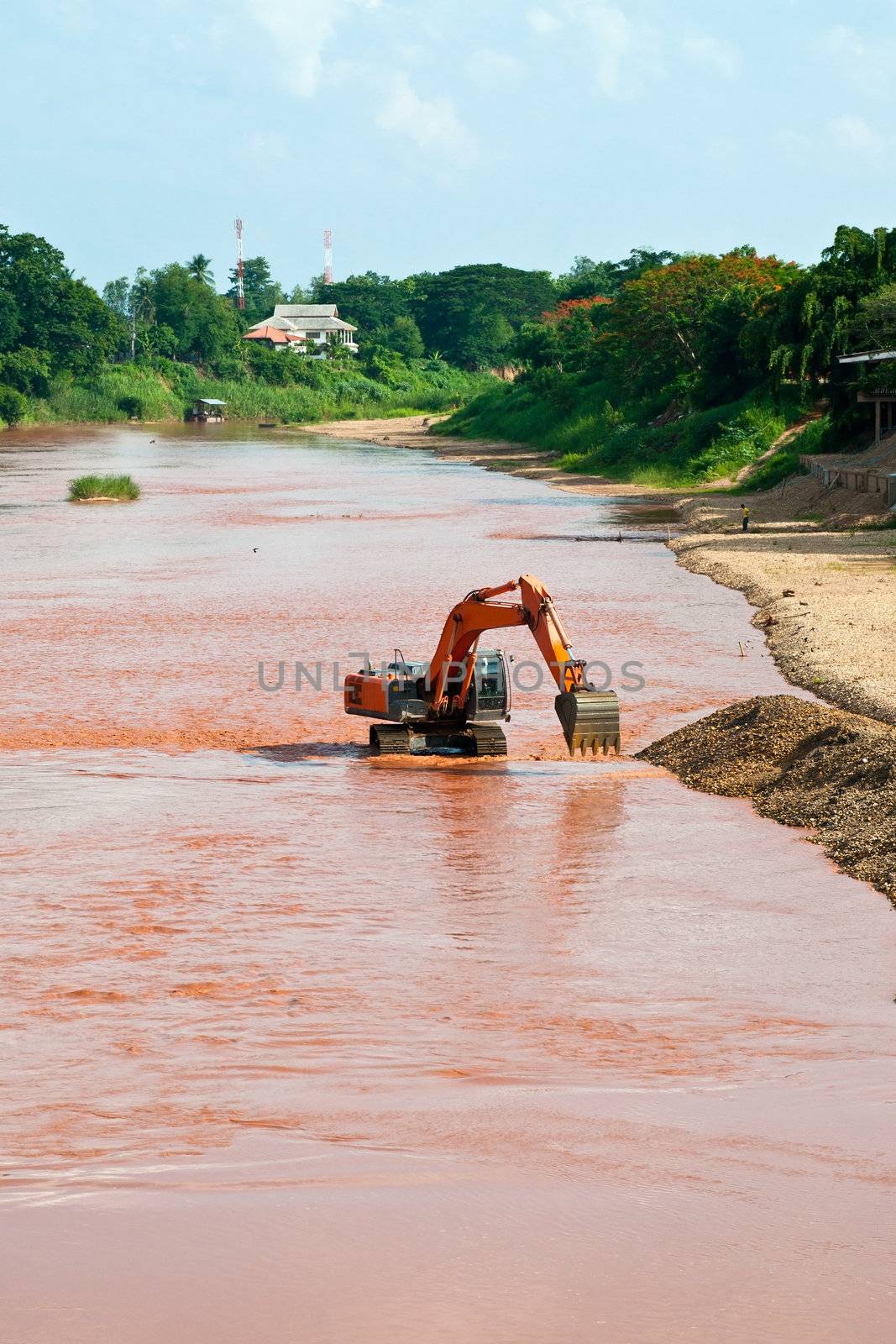 Excavator loader at river with raised bucket over blue sky