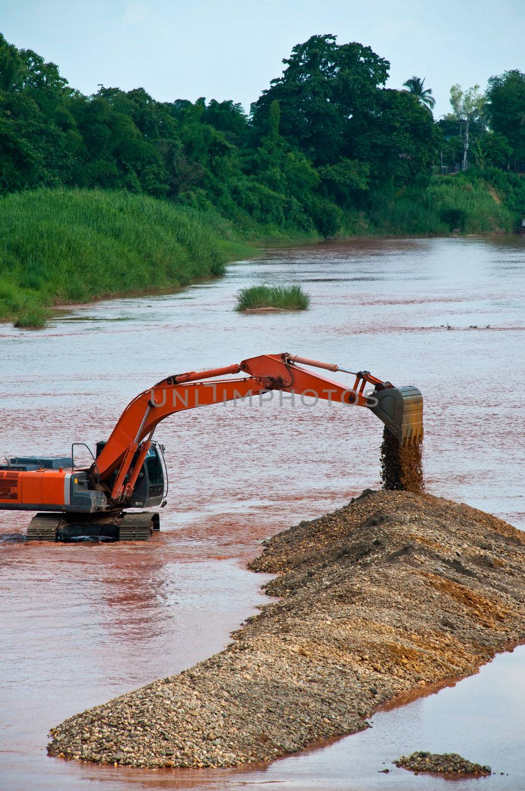 Excavator loader at river with raised bucket over blue sky by Yuri2012