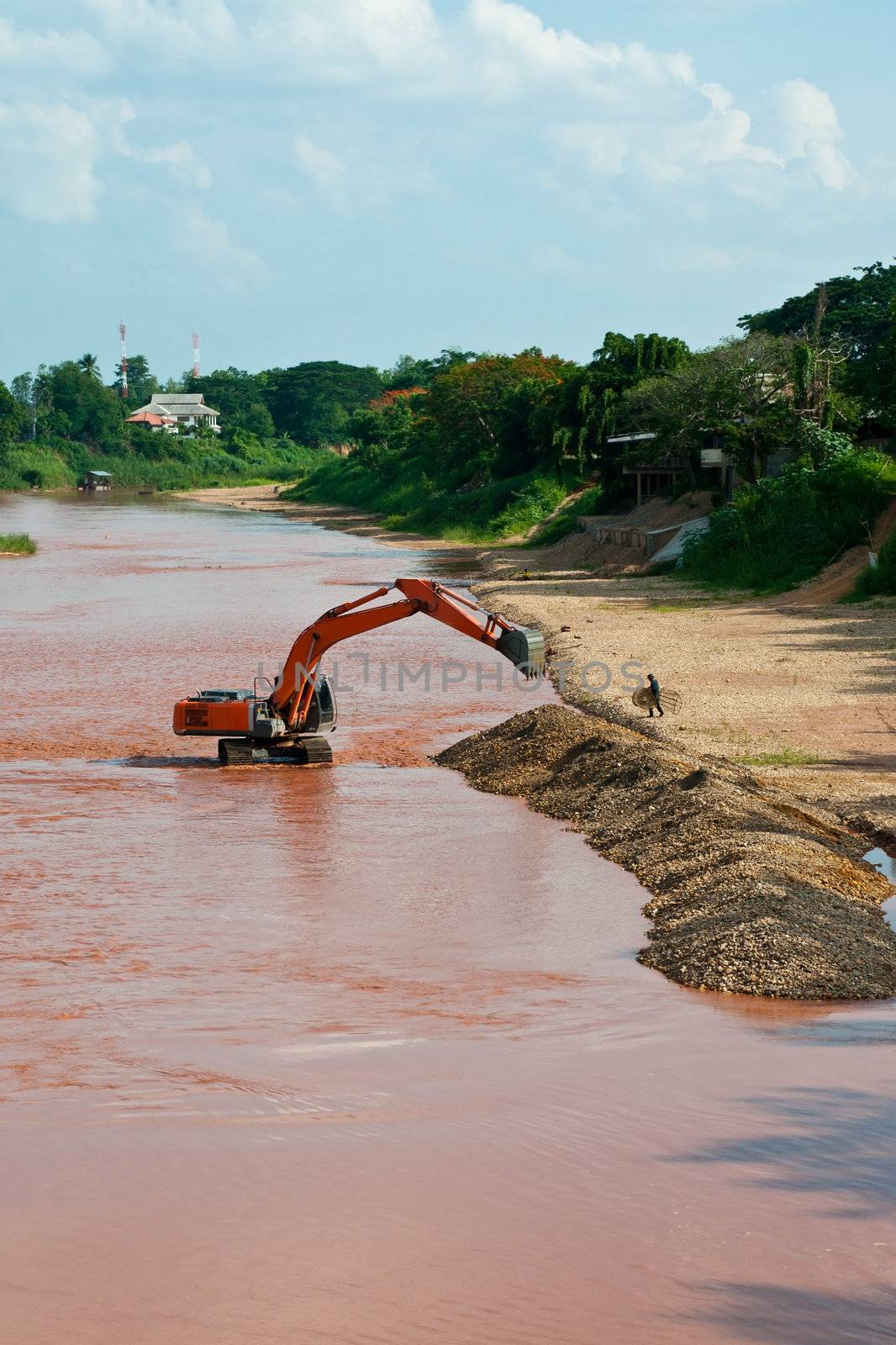 Excavator loader at river with raised bucket over blue sky