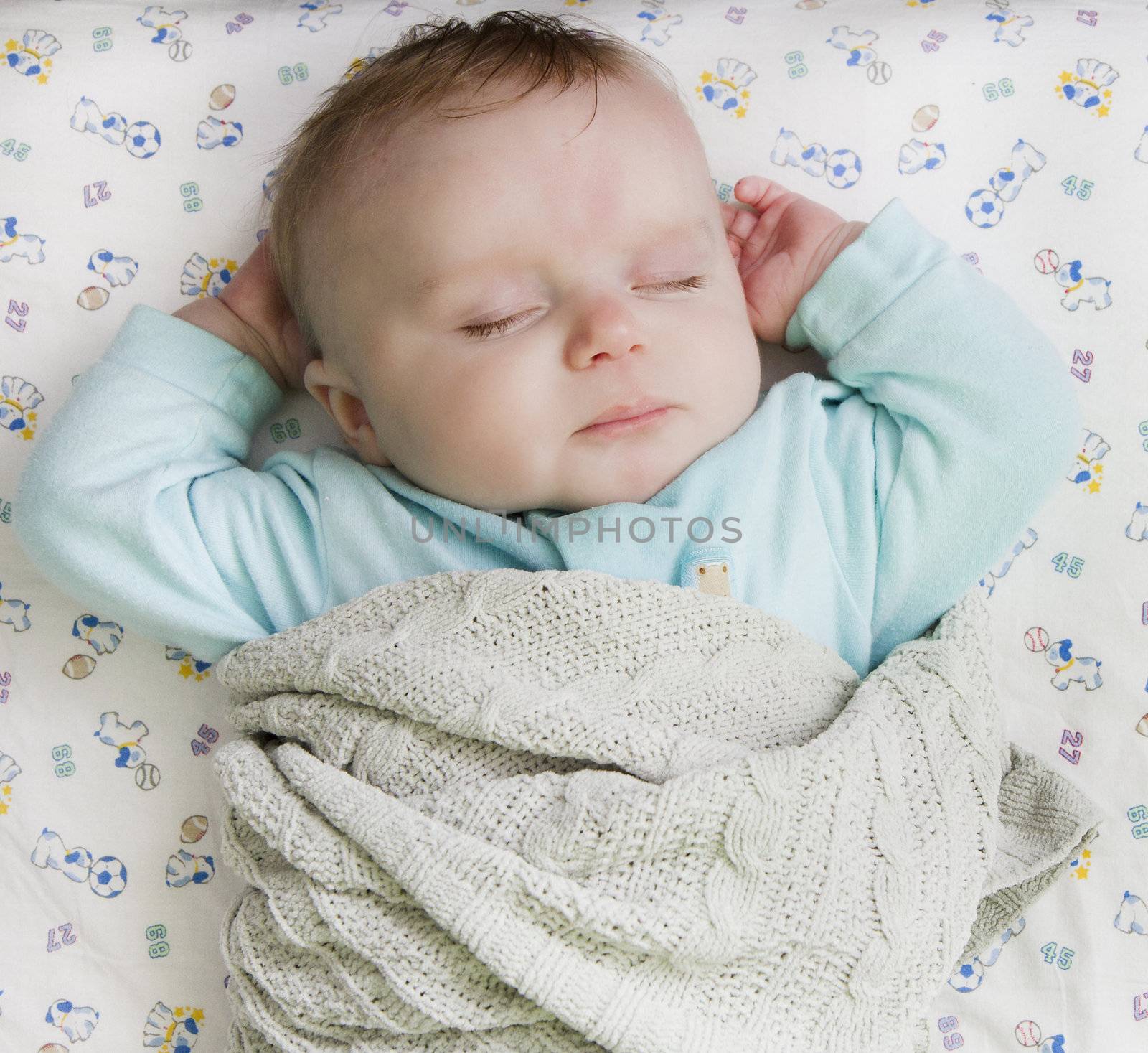 Infant laying on his back on a bed with his hands up near his head