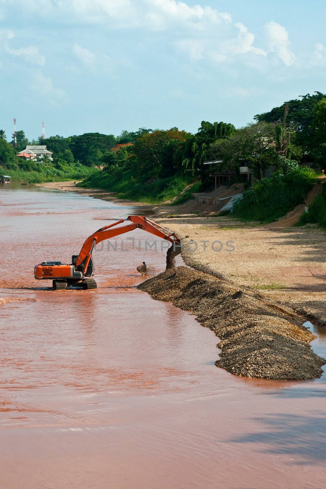 Excavator loader at river with raised bucket over blue sky