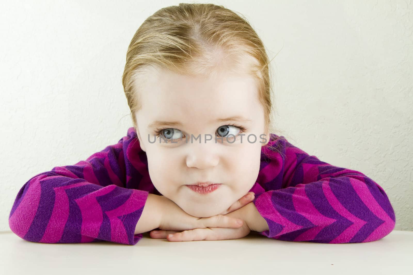 Head on view of a young girl resting her head on her hands at the table while looking away from the camera