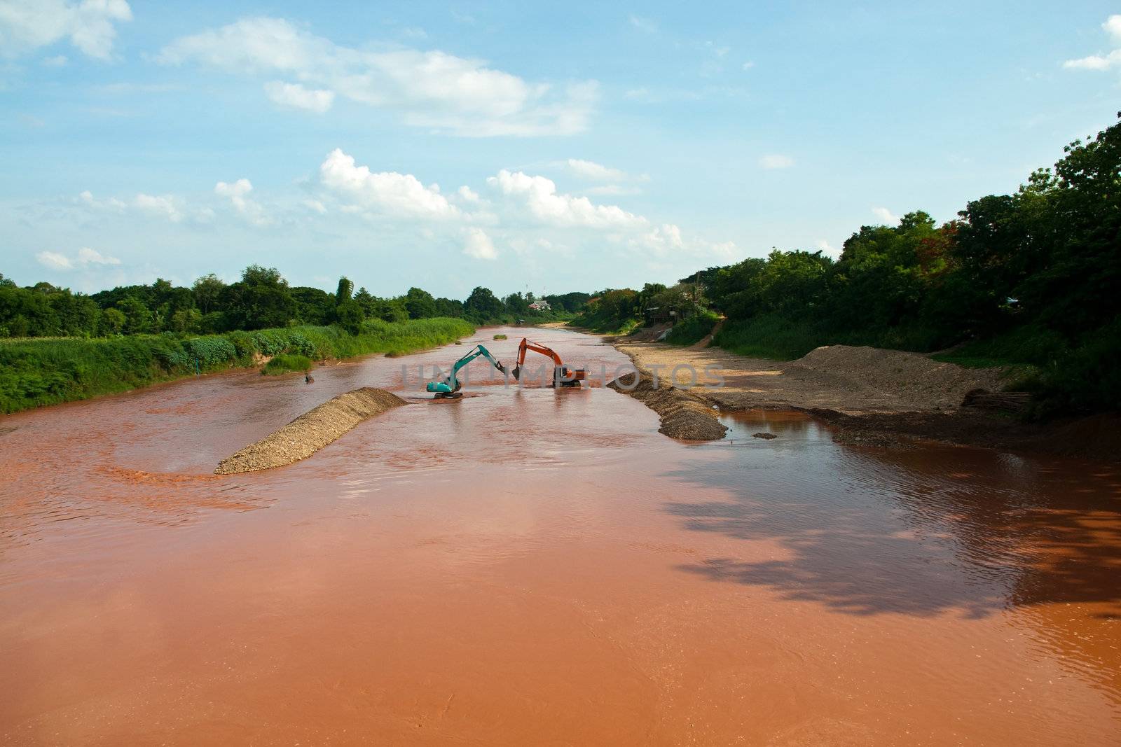 Excavator loader at river with raised bucket over blue sky