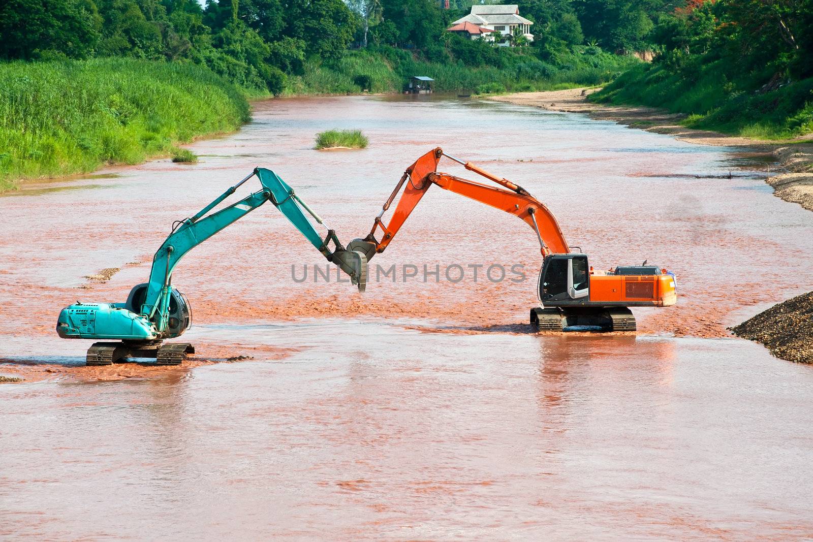 Excavator loader at river with raised bucket over blue sky