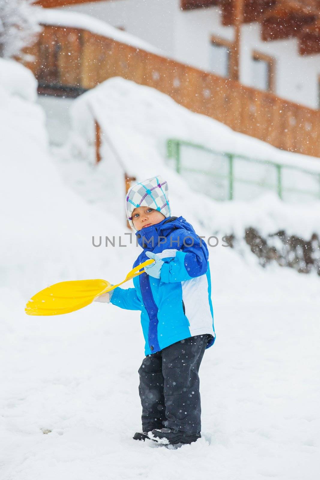 Cute little boy in blue riding on a sled near  the Austrian cottage