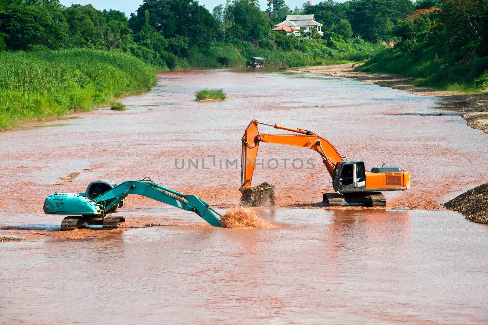 Excavator loader at river with raised bucket over blue sky