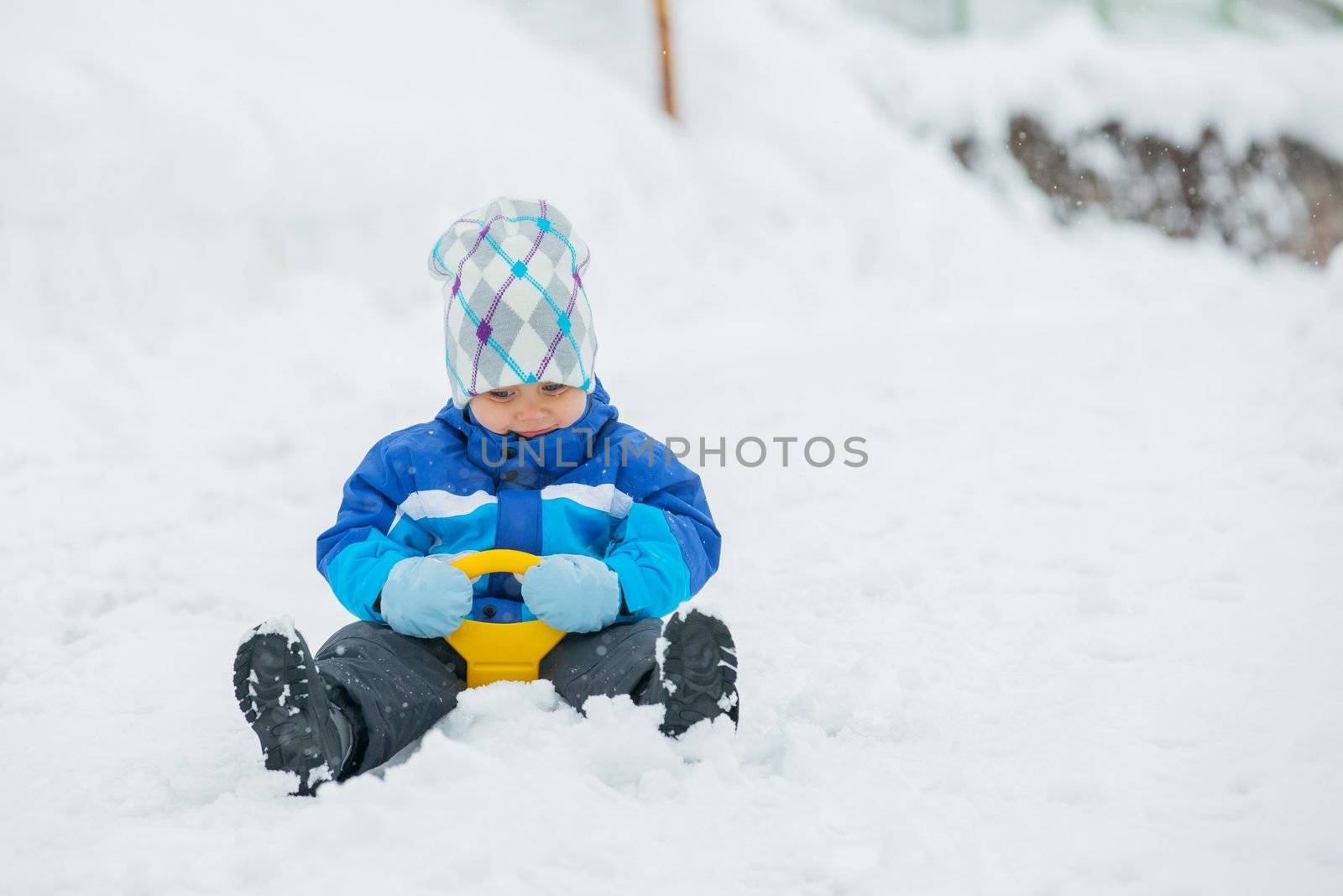 Cute little boy in blue riding on a sled near  the Austrian cottage