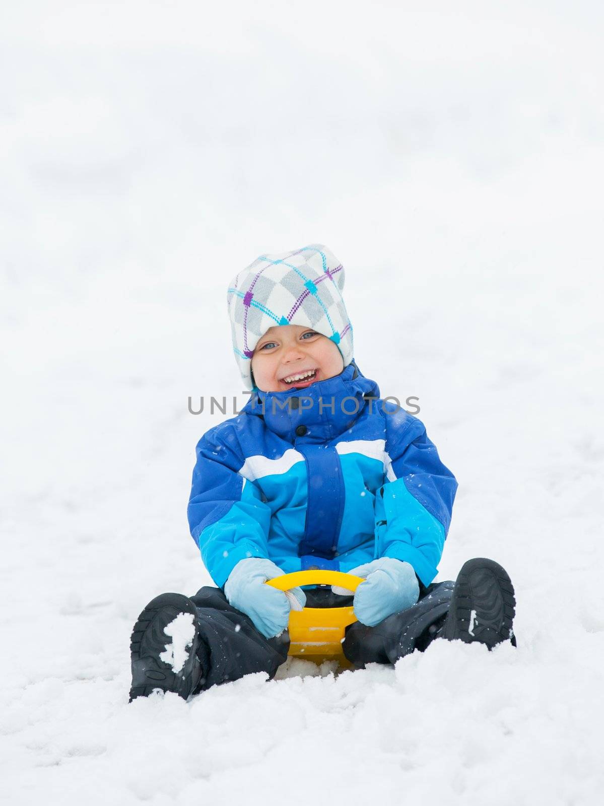 Cute little boy in blue riding on a sled near  the Austrian cottage