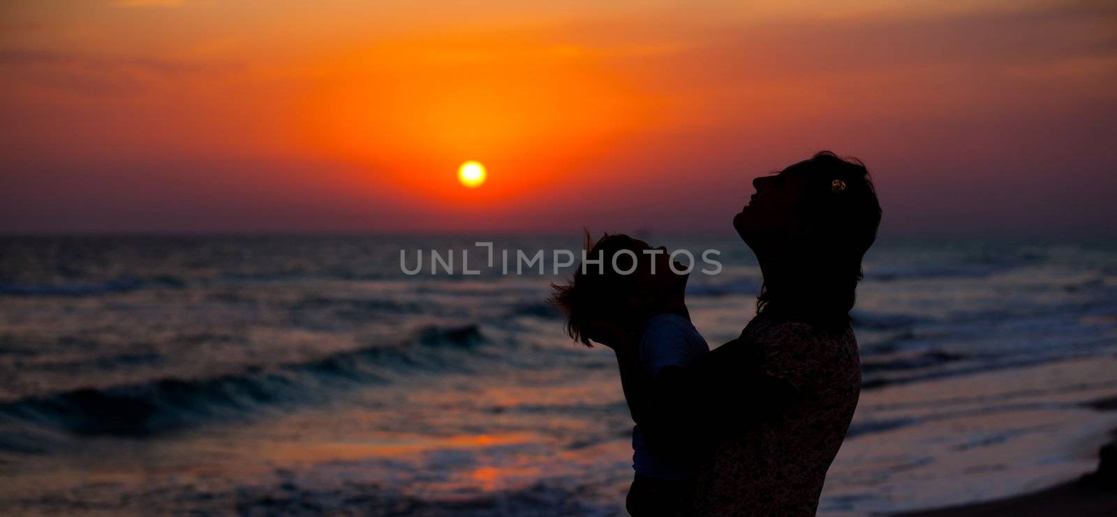 Mother and little son silhouettes on beach at sunset