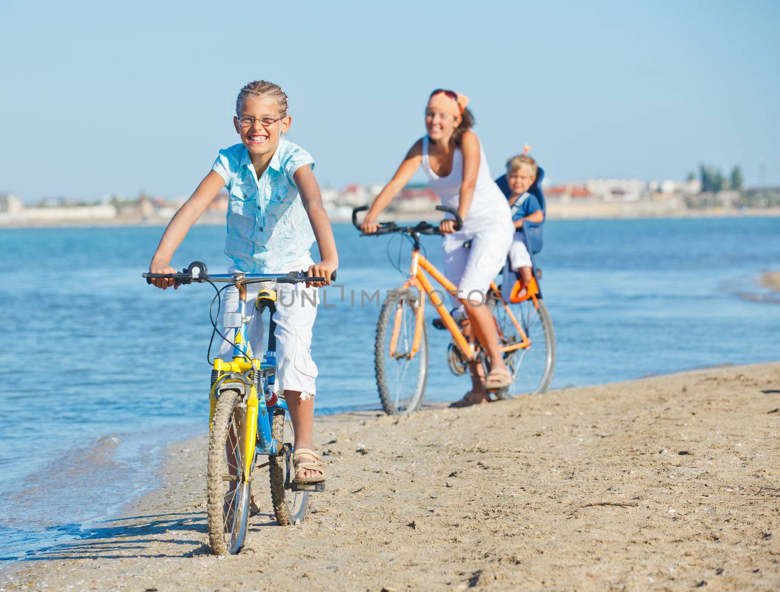 Cute girl with her mother and brother ride bikes along the beach. Focus on mother