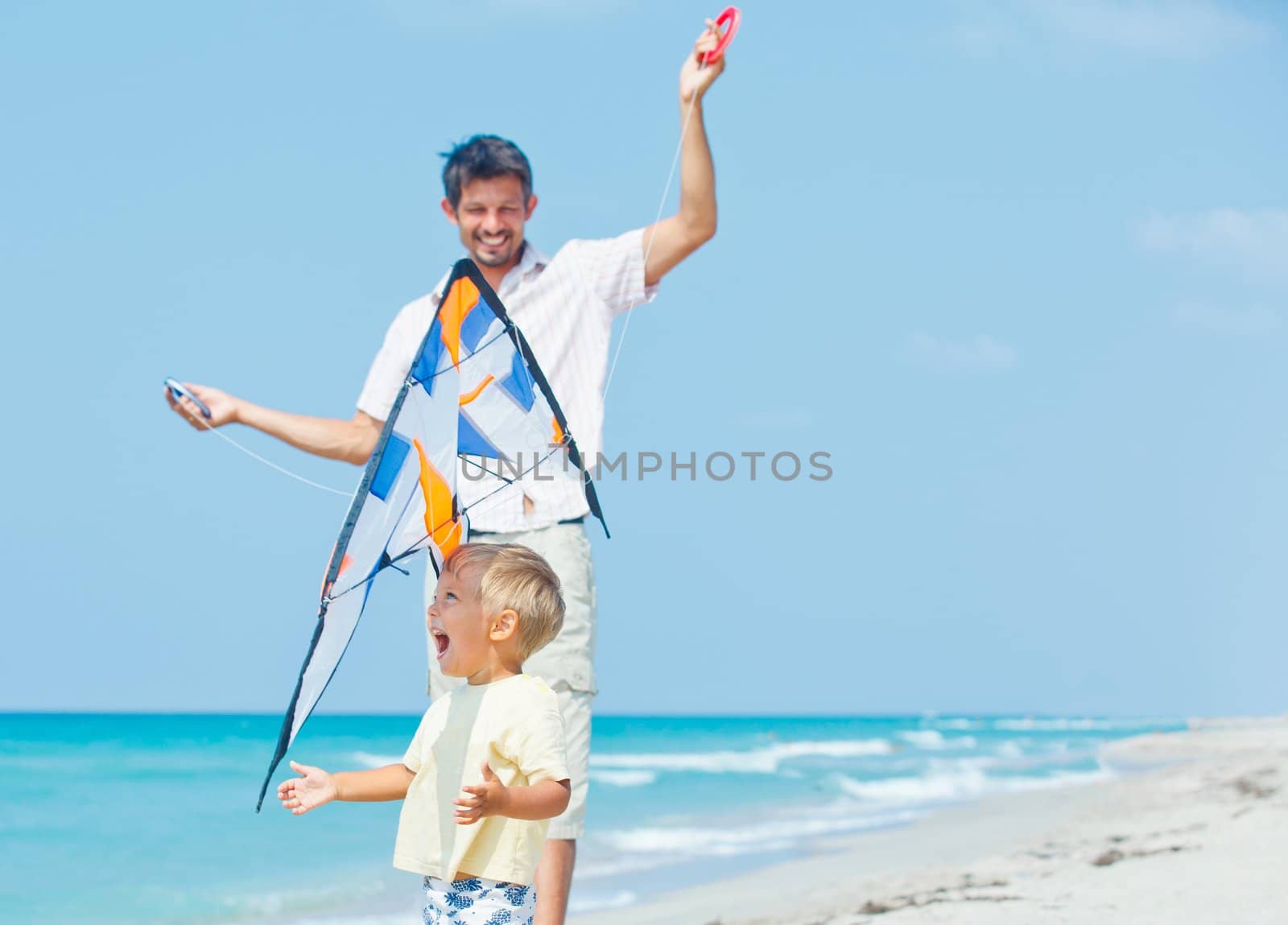 Little cute boy playing his father with a colorful kite on the tropical beach.