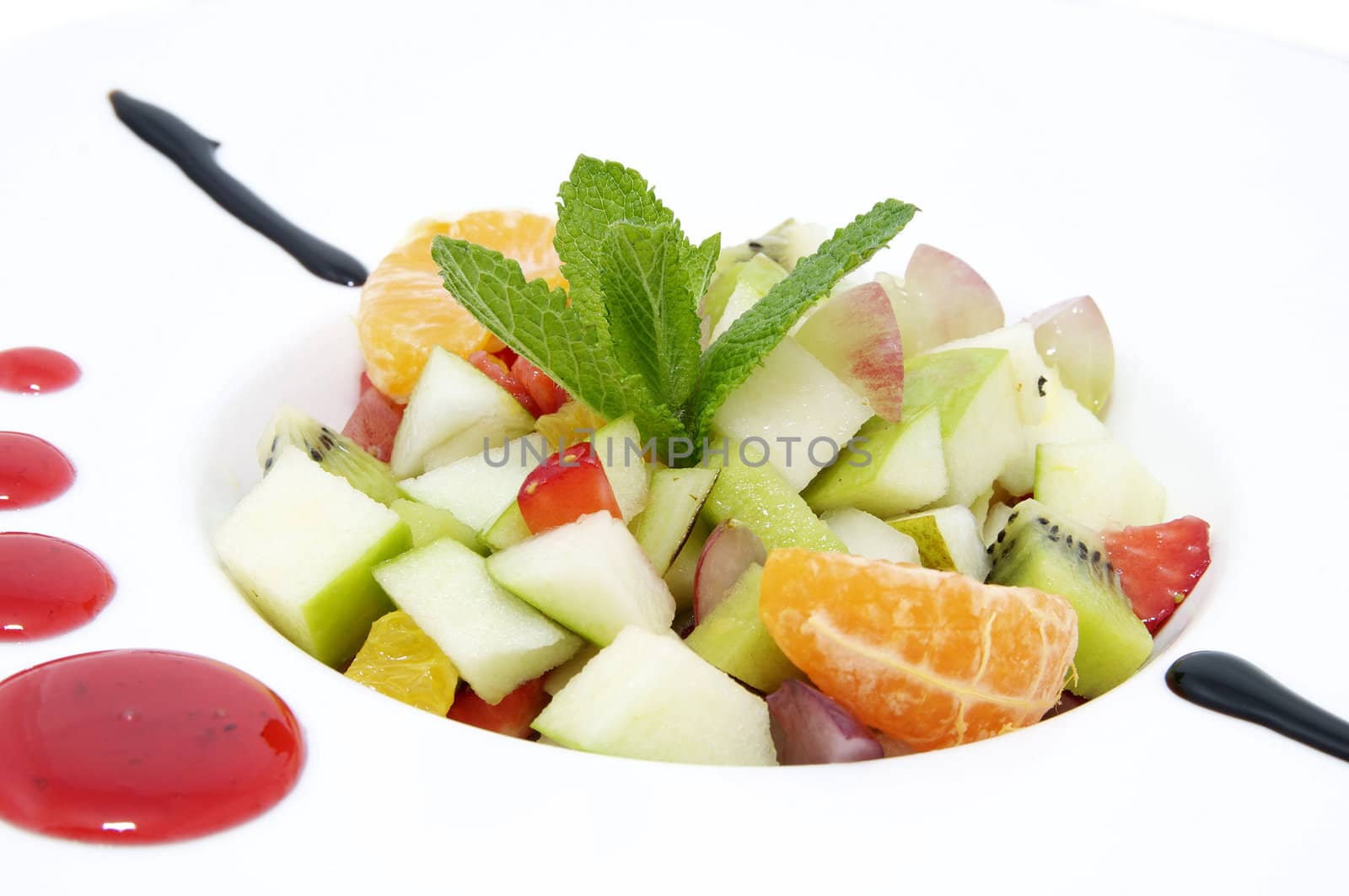 fruit salad decorated with mint on a white plate