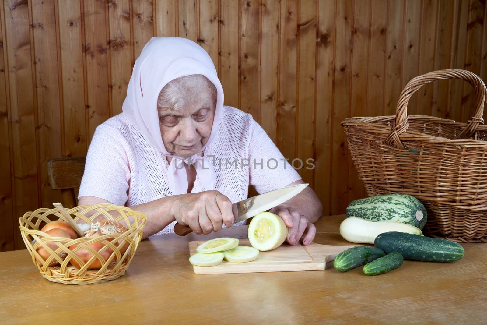 The old woman cuts  vegetable marrow on a table