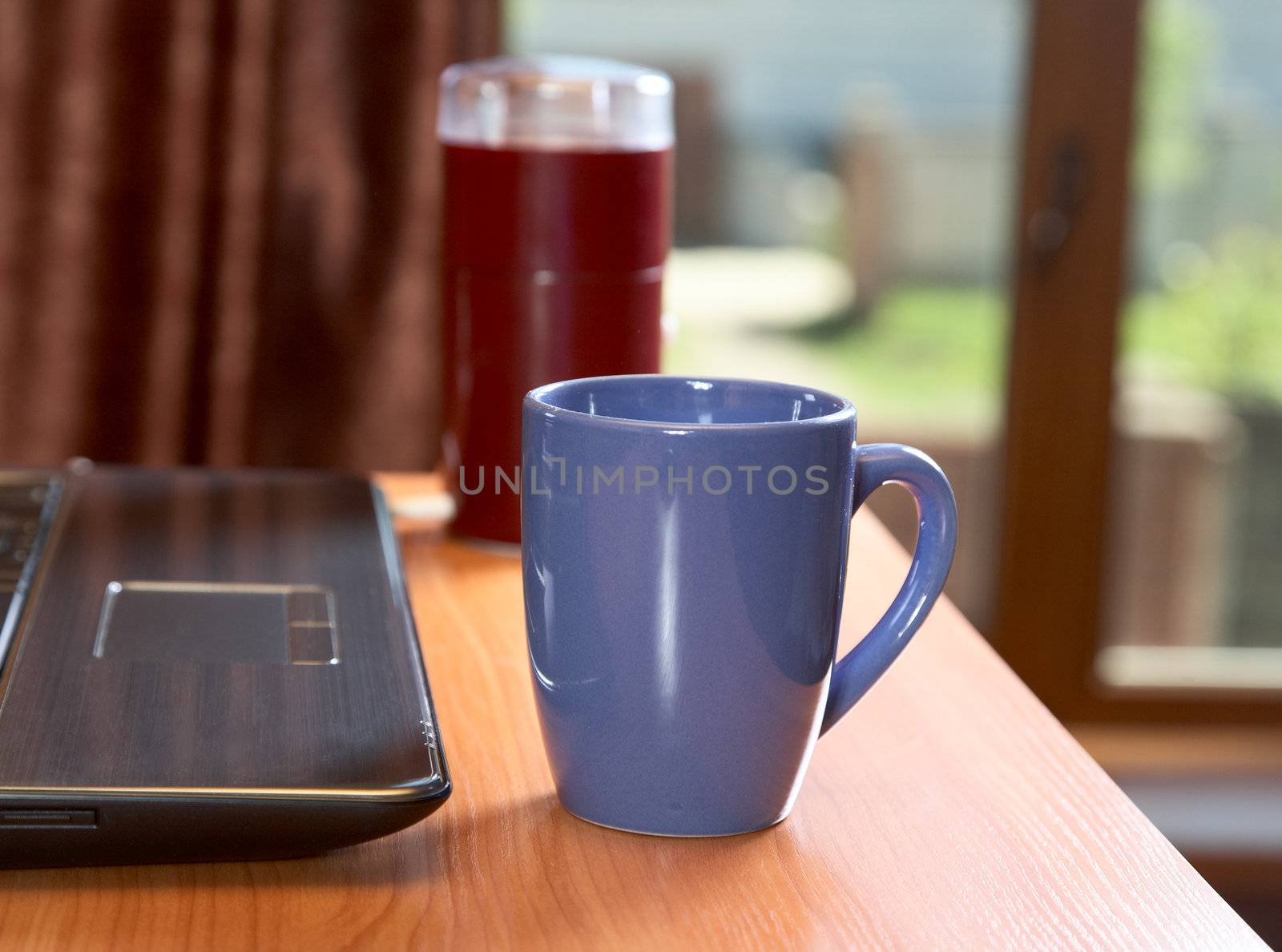  laptop coffee grinder and  cup on a desk in the solar morning