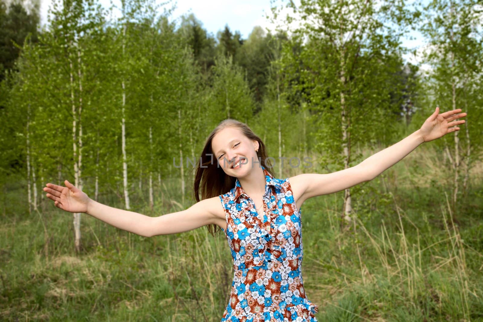  girl has widely stretched hands against young birches in the spring