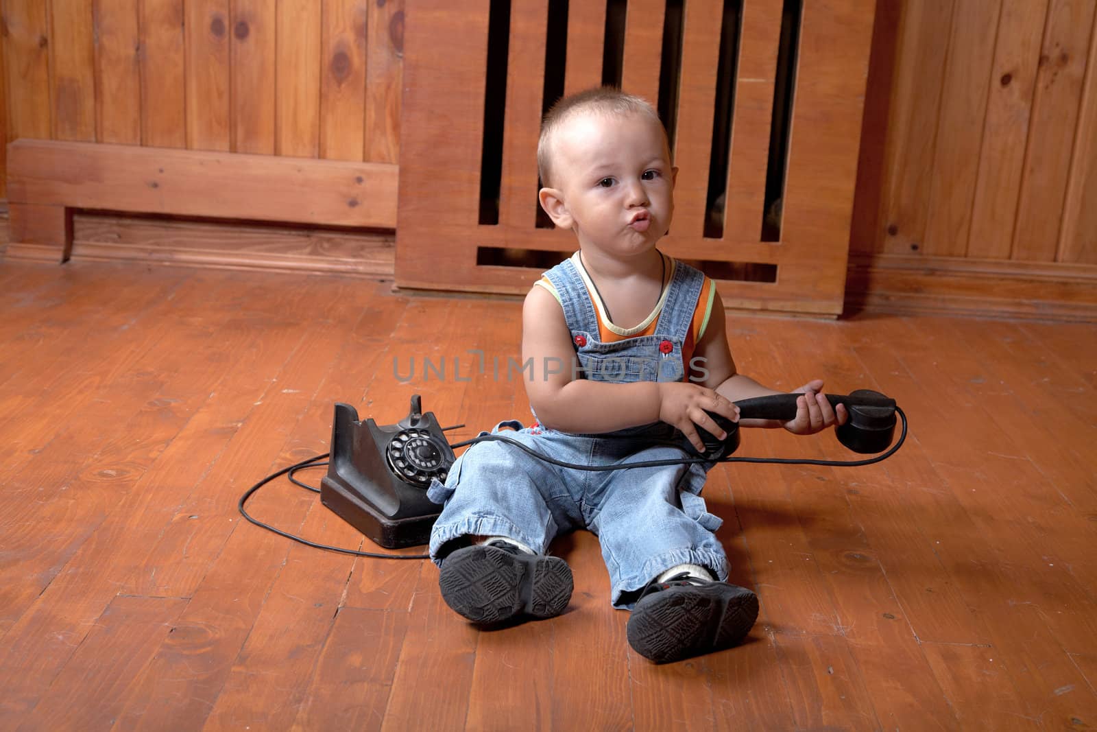 The little boy plays old phone sitting on a floor