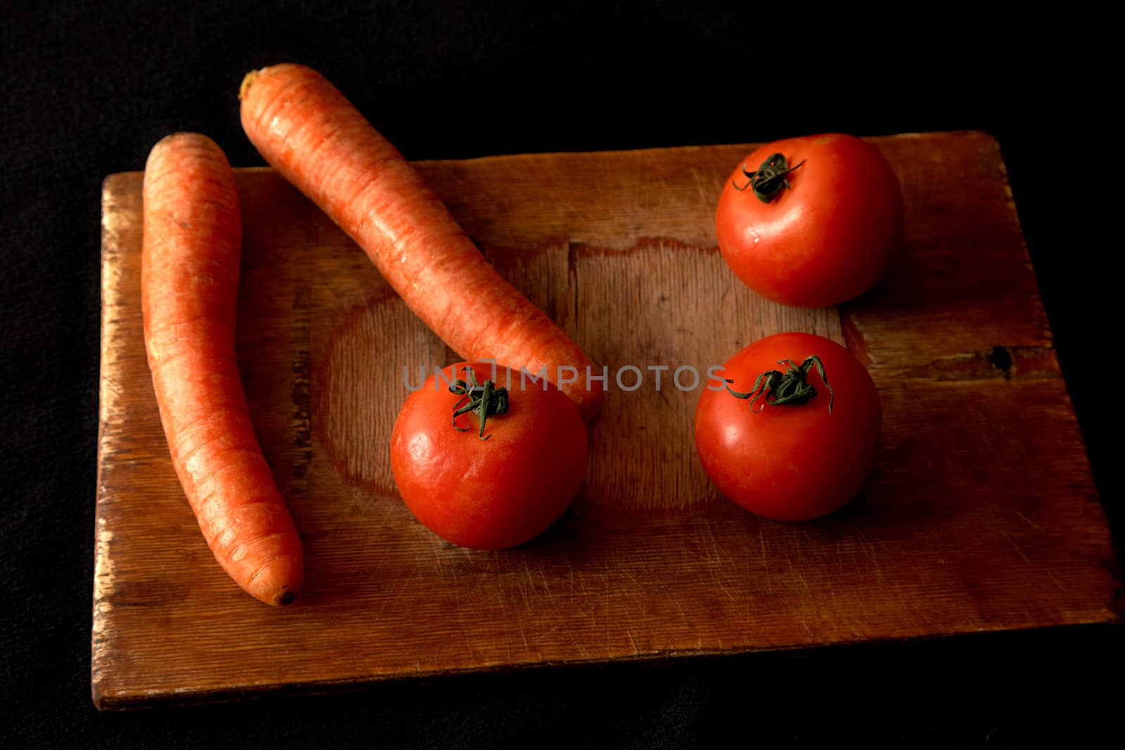 Carrots and tomatoes on an old chopping board a black background