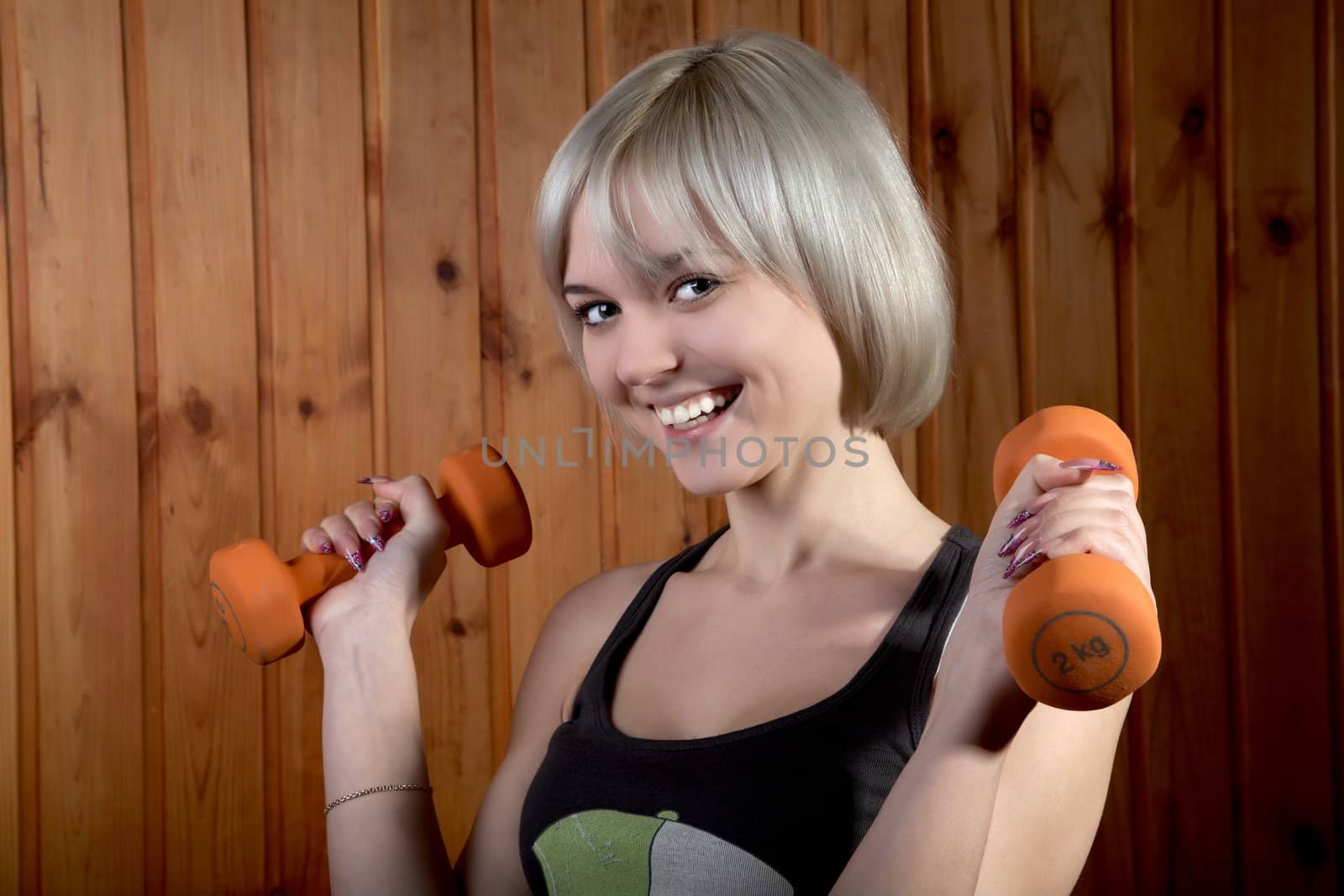 The cheerful girl with dumbbells against a wooden wall