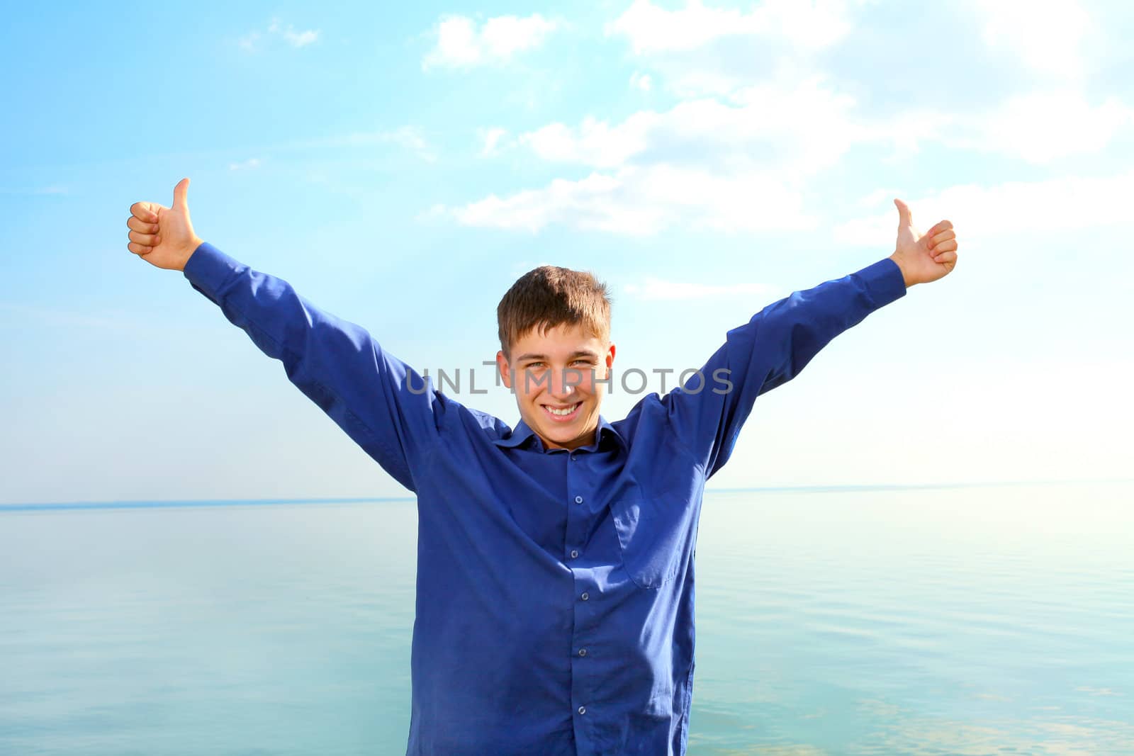 happy young man spread hands with thumbs up on the seaside background in the sunny day