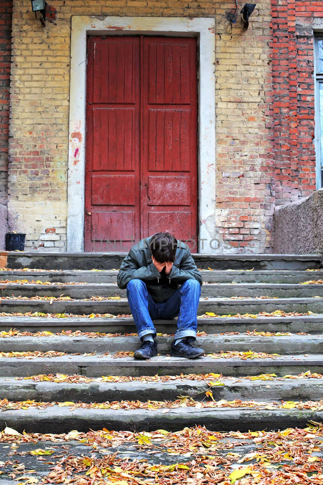 sad young man with hidden face on the old house background