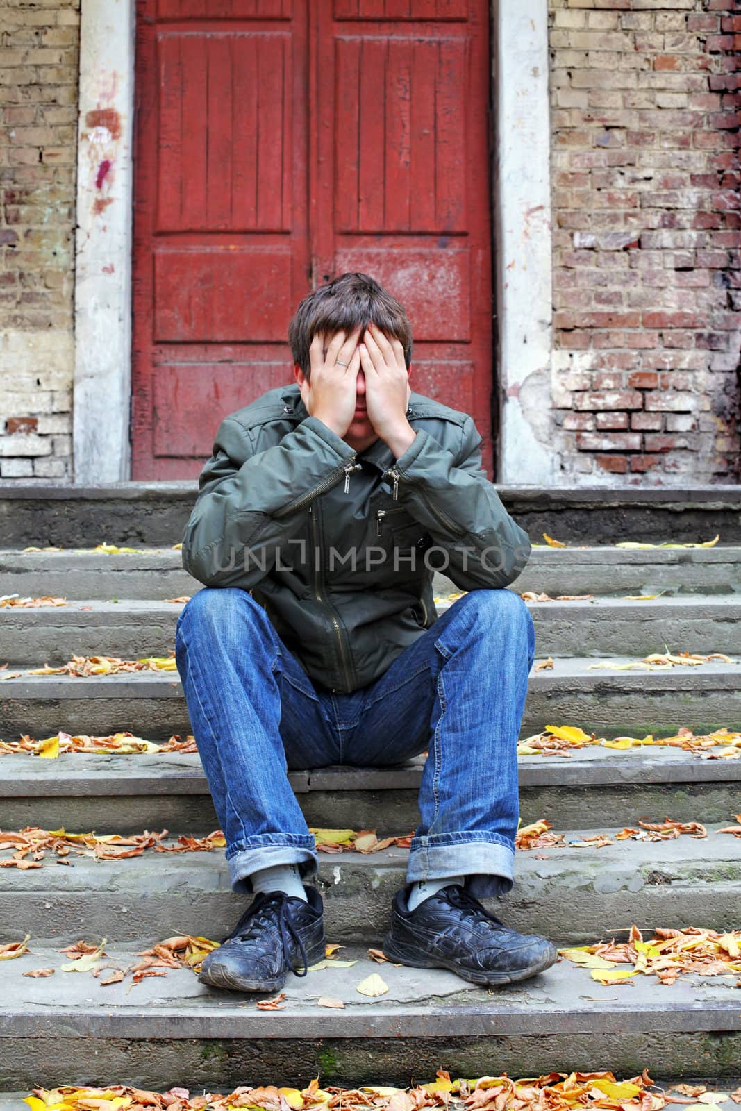 sad young man with hidden face on the old house background