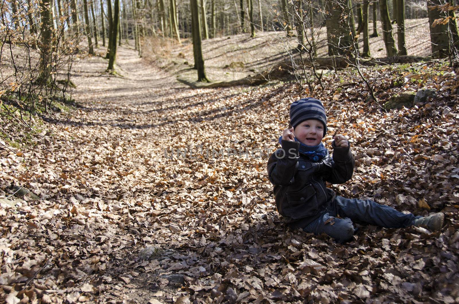 Young boy on forest floor in spring playing with leaves