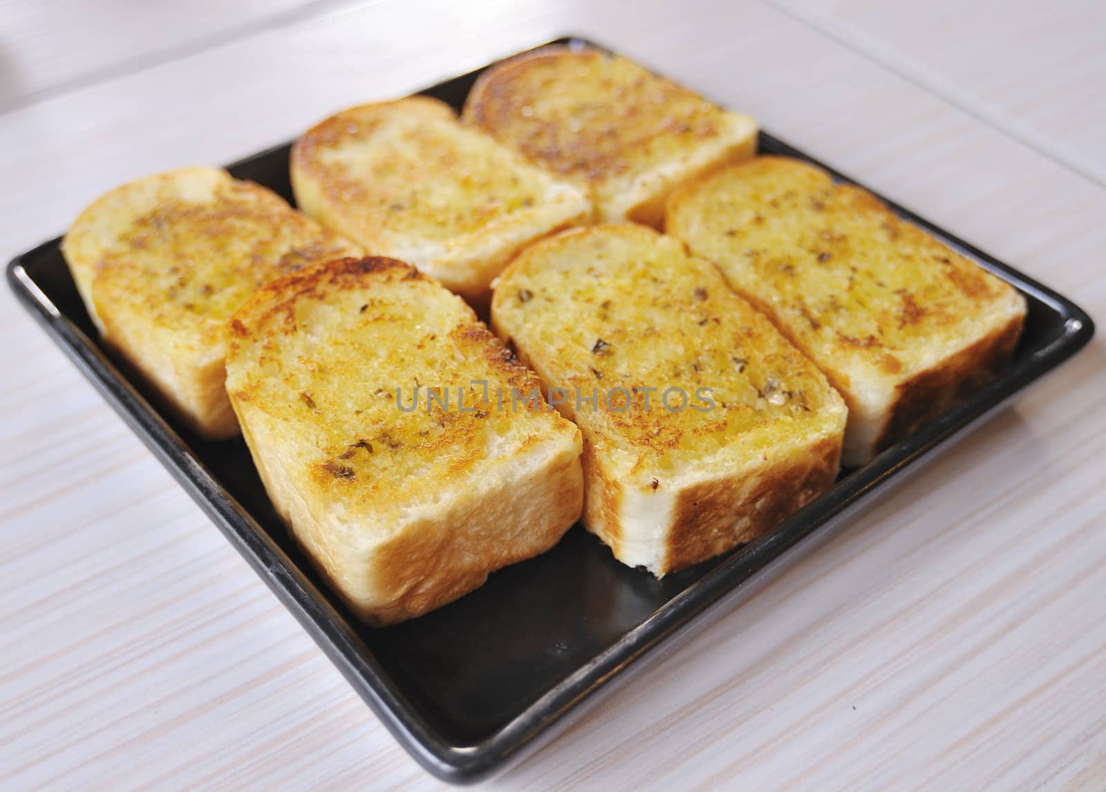 Garlic bread with herbs, on black bread dish. by sommai